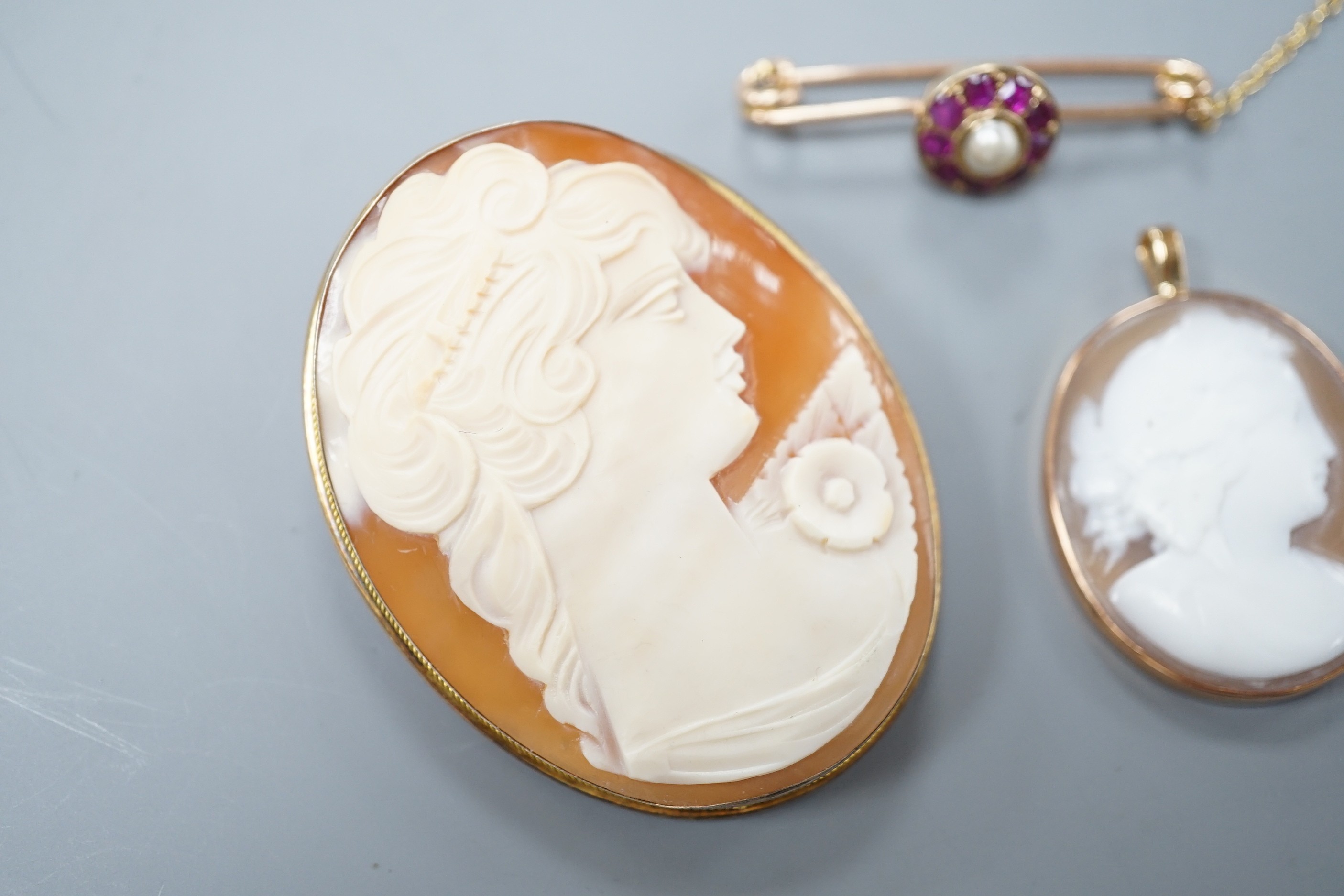 A 9ct mounted oval cameo shell pendant, 36mm, a similar gilt white metal mounted brooch and a yellow metal, ruby and cultured pearl cluster set bar brooch(converted).